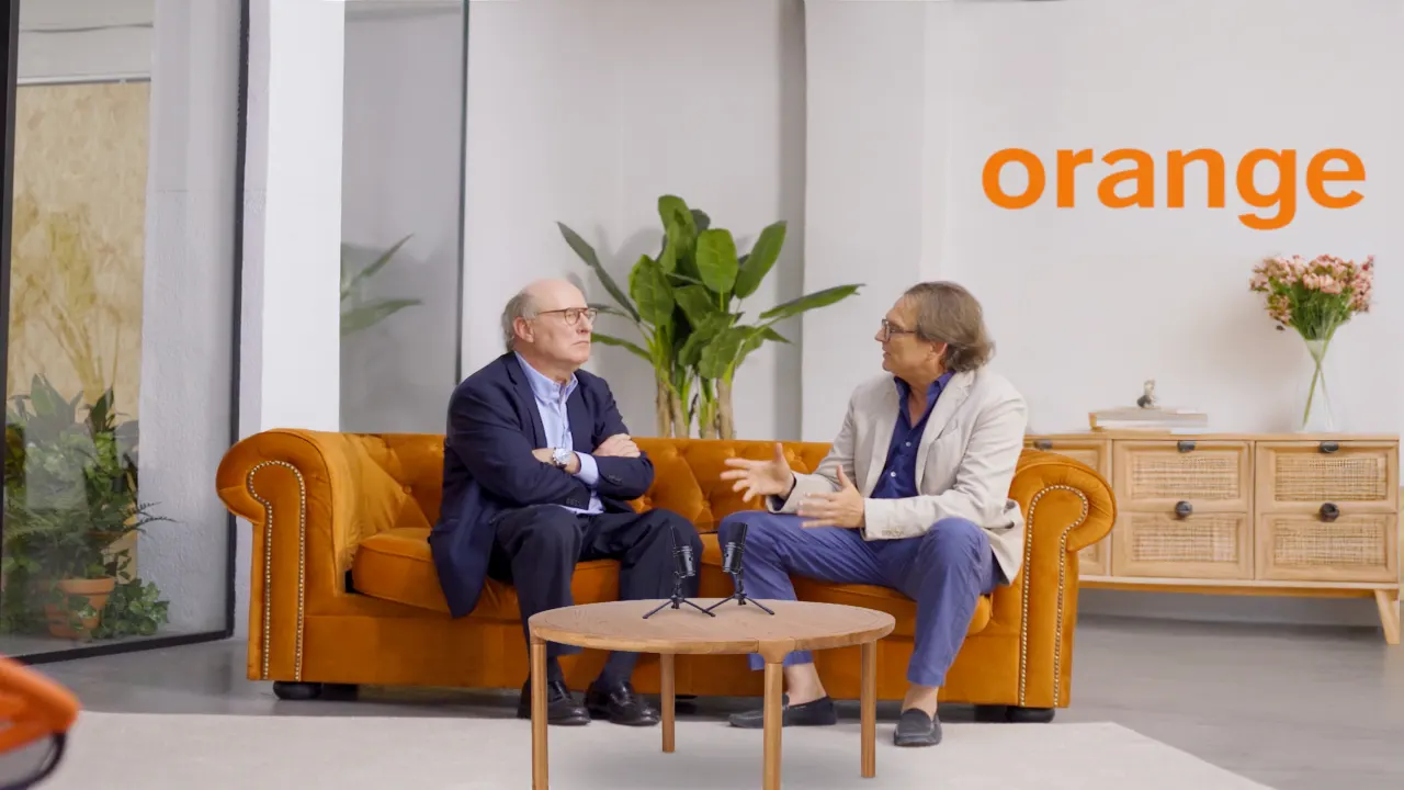 Dos personas conversando en un sofá naranja en un set de marca de Orange